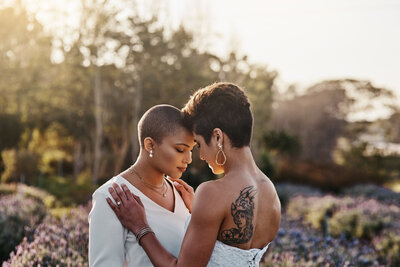 Two brides standing close together with their foreheads touching.