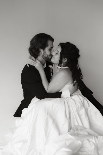 A couple sitting closely together, sharing an intimate embrace in soft studio light.