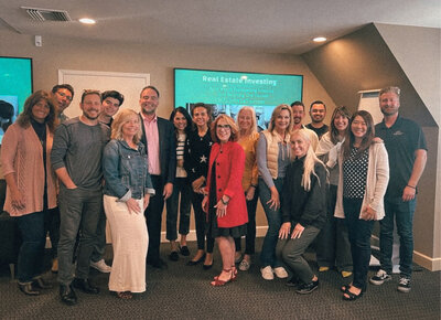 Carolynn Santaniello standing with a group of attendees at a real estate investing workshop in a conference room setting.
