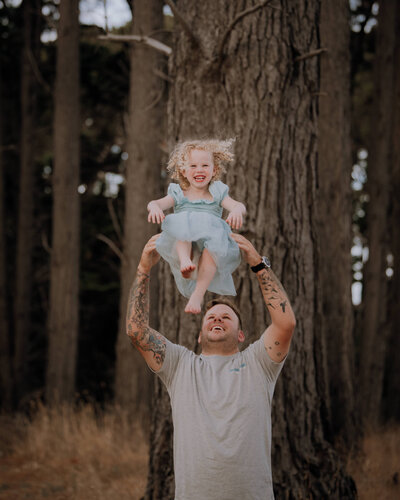 Dad tossing daughter up in the air as she laughsin a woodland setting