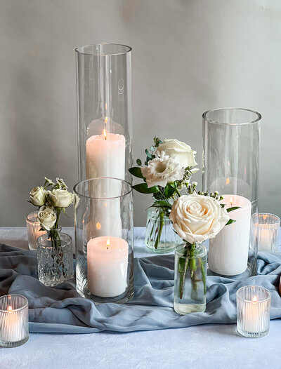 Group of clear bud vases with white flowers and candles on a table