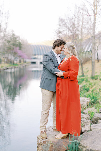 couple cuddle close for engagement pictures at river in Bentonville, Arkansas