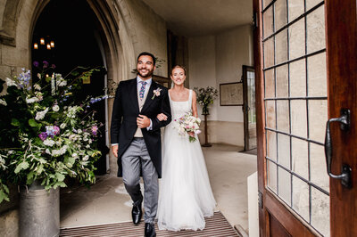 Bride and groom exiting Painswick Church with a Churn of flowers in the background