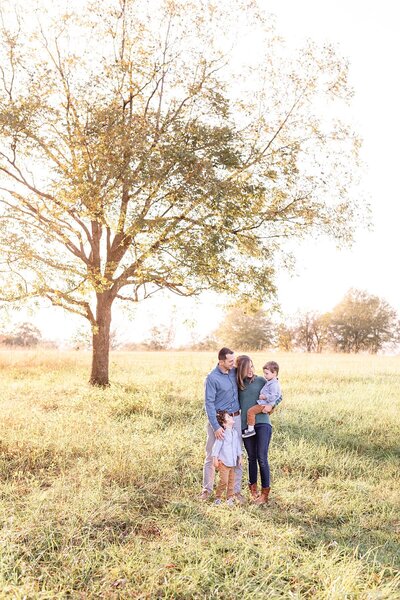 Mom and dad holding toddler brothers in front of tree in field at Hopkins Farm at sunset