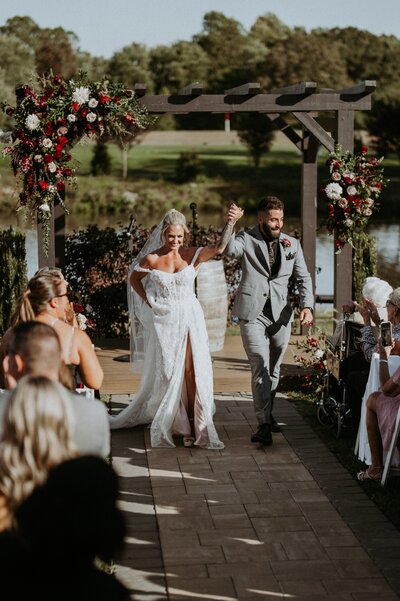 Romantic wedding altar with fresh floral arrangements by Leigh Florist, highlighting roses, ranunculus, and greenery in a classic outdoor ceremony setting.