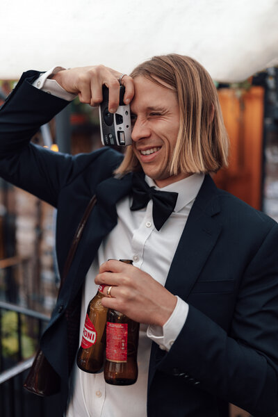 Groom smiles and takes a picture with a film camera of his wife at a central London wedding ceremony