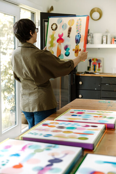 An artist examining a colorful abstract painting in her vibrant studio, surrounded by tools and completed artwork for a creative branding session.