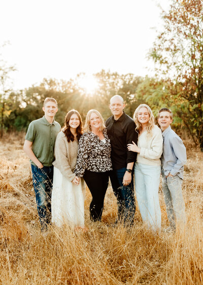 Backlit photo of a family of 6, parents and 4 grown children in a dry field.
