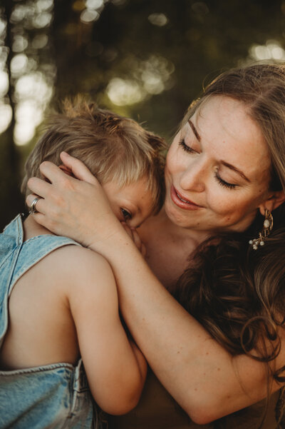 A mother holding her toddler boy and playing with his hair.