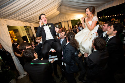 bride and groom being help up on chairs during reception