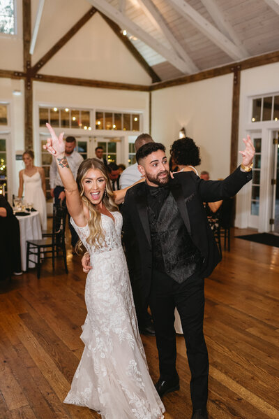 Wedding reception photo at Bear Creek Mountain Resort wedding venue in Macungie, Pa. The groom is picking up the bride and spinning her in celebration of their entrance into their wedding venue while guests cheer around them. The bride and groom are both holding beers and throwing them up in celebration as they share a kiss. Pa wedding reception photos, Pa wedding photos, Pa wedding photographer.