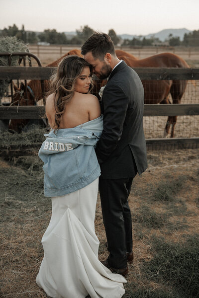 couple embrace next to horse pen after wedding in san diego