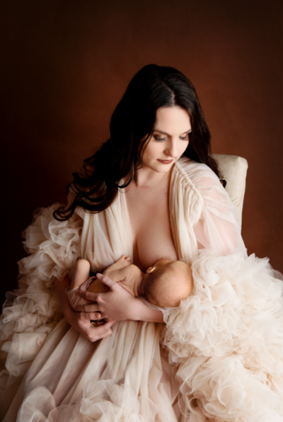Breastfeeding mom wearing a white luxurious gown  for her maternity shoot in St Louis MO