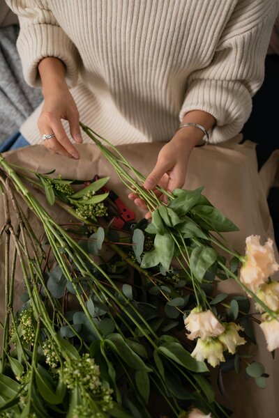 A woman in a tan sweater arranging flower stems