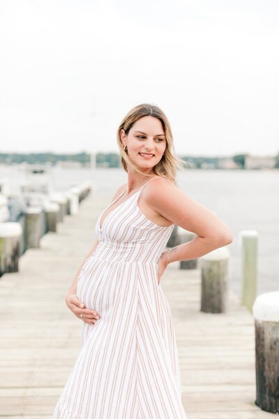 A woman wearing a white dress and holding her pregnant belly during portraits in NJ