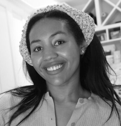 Black and white photo of wearing a handkerchief in her hair, smiling vibrantly at the camera.