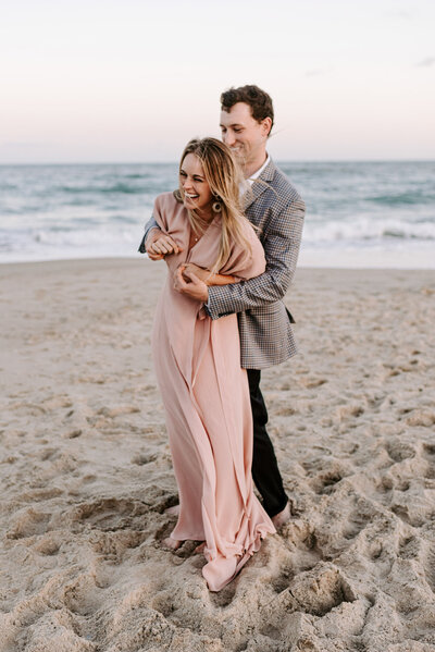 man and woman embracing and smiling while standing on beach