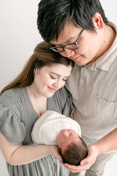 Mom and Dad snuggling together while holding newborn baby in their arms at Portland Oregon newborn photography session.