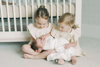 two toddlers holding their newborn sibling