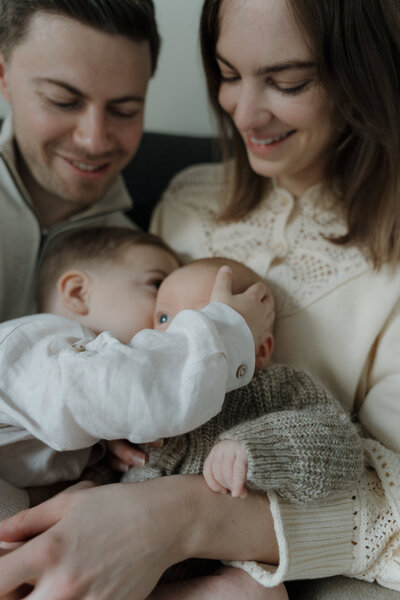 Moeder en vader knuffelen op bed en houden hun 2 kindjes vast waarvan een baby.