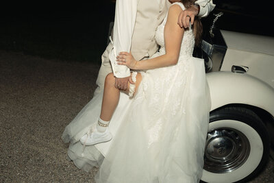 Bride and groom night photo of a classic car, bridal sneakers and a garter