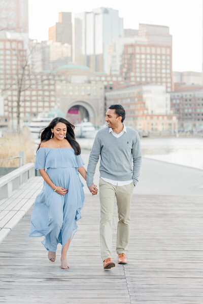 A pregnant woman and her husband laugh and walk at Boston Seaport