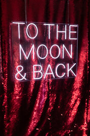 To the moon and back neon sign against a red sequins backdrop