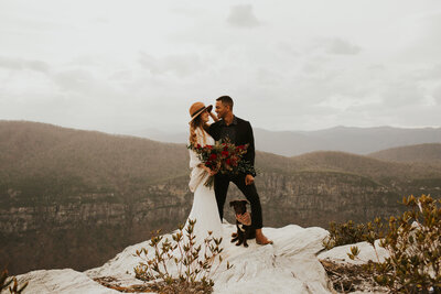 bride and groom standing on cliff with mountains in background