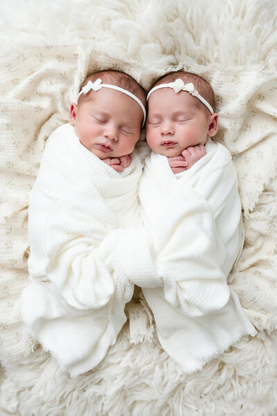 This sweet newborn twin photography session in Pittsburgh captures two precious babies wrapped in soft white fabric and adorned with matching bow headbands. Their peaceful slumber and tender poses reflect the beauty of twin newborns during their early days.