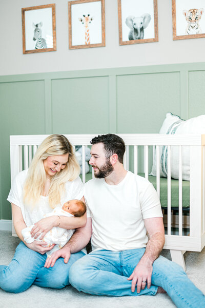 Couple sitting on the  floor in front of a crib holding their newborn