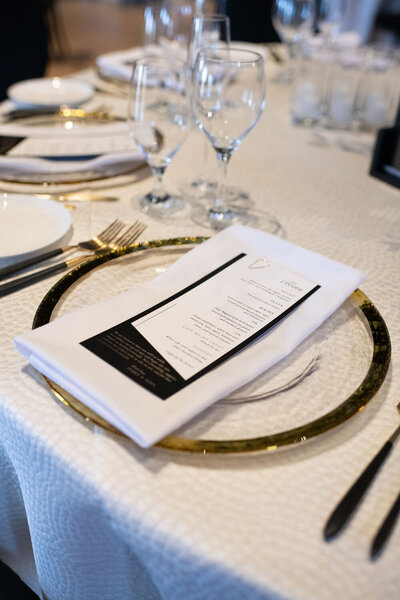 Two-layer wedding menu with a gold paper clip accent placed on a white napkin and a gold and glass charger at a spring wedding at the Palm Event Center in Pleasanton, CA.