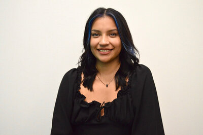 A portrait of Marilyn Carmona, a stylist at 212 Salon, Spa, & Barbershop, wearing a black top and smiling at the camera.