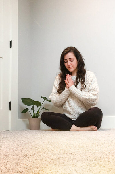 person sitting on the ground with her hands together and eyes closed