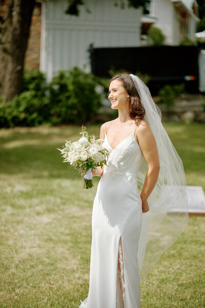 Bride standing in the sunlight smiles to someone off frame