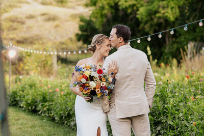 Groom gently kissing his bride on the forehead during their wedding at Lyons Farmette, in Lyons, Colorado, capturing a tender and intimate moment.