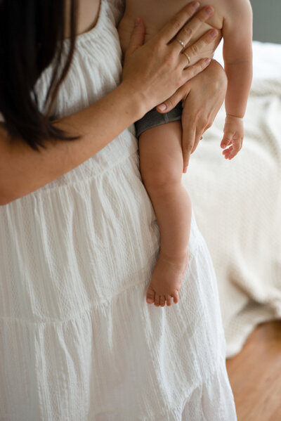 A mom wearing a white dress and holding a baby on her hip