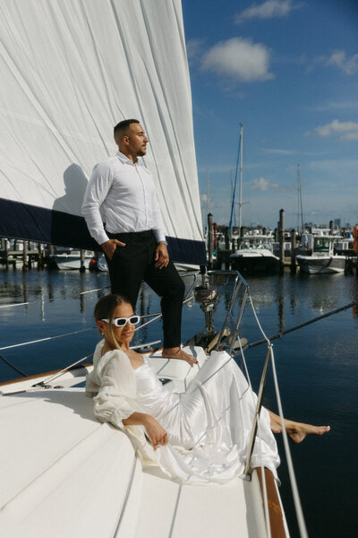 Bride and groom sitting on a sailboat in Miami Florida the morning of their wedding for sunrise portraits, by Andrea-Marie Photography