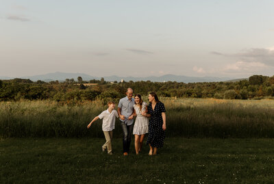 A family portrait of the parents and two kids in a picturesque Vermont field at golden hour.