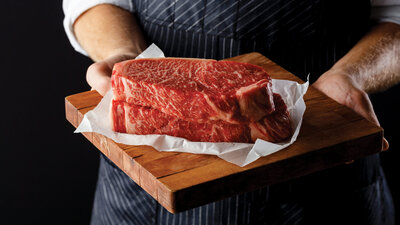 Hands holding two large raw Omaha Steaks on butcher paper and a cutting board. 
