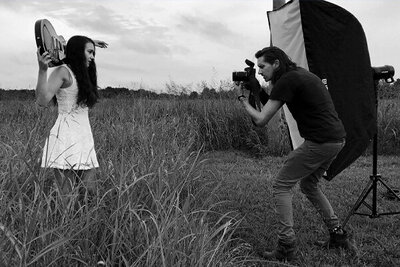 Country Music Photography Nashville Behind the Scenes Photo Mark Maryanovich photographing Leanne Pearson black and white artist standing with guitar resting on her shoulders wearing white dress Mark standing beside flash