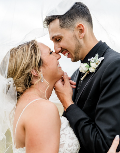 Bride and groom sharing an intimate moment with their noses touching, smiling under the bride's veil