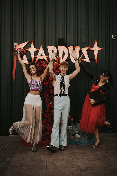 People in wedding attire in front of neon Stardust sign