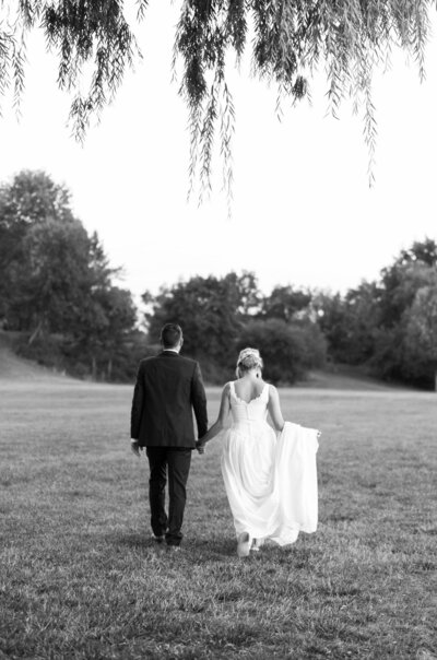 married couple hold hands and walk towards the tree line at sunset