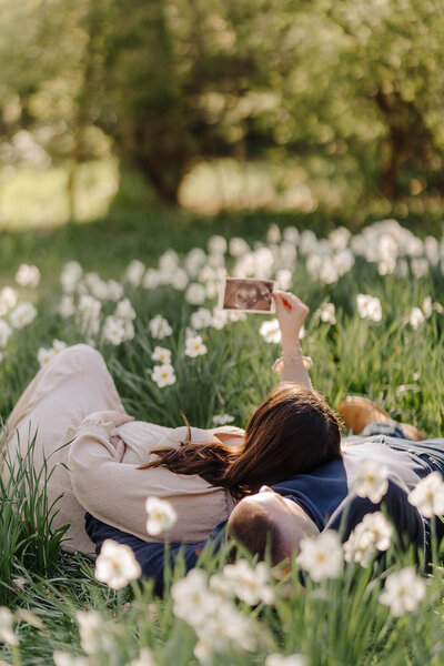 Woman laying down in flowers holding a photo in the air