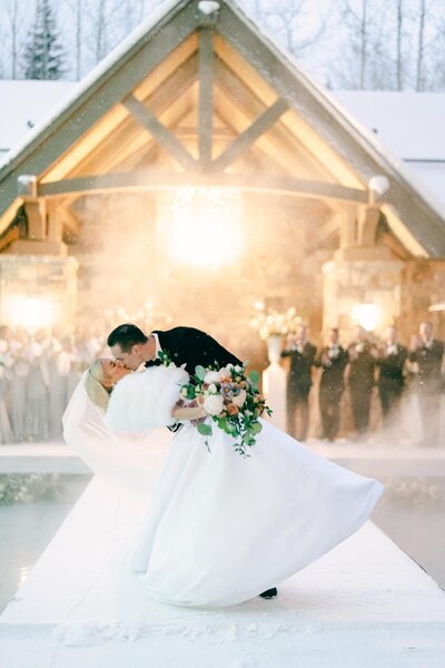 Romantic moment of newlyweds kissing in the snow at the Four Seasons Vail, captured during a dip kiss in the aisle