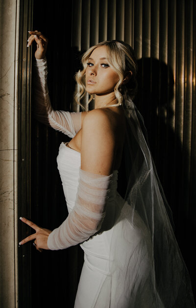 woman wearing white bridal gown while leaning against a wall