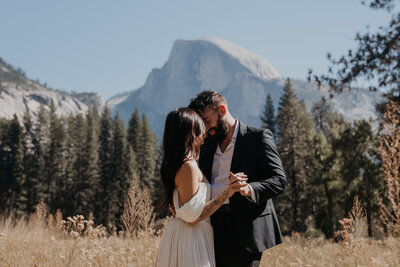 close up of bride and groom dancing and holding hands during their first dance after their elopement in Yosemite behind them are lots of trees and half dome