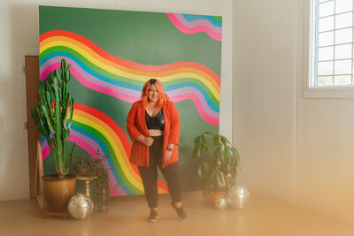 Image of a person smiling while standing in a front of a wall with a mural painted on it