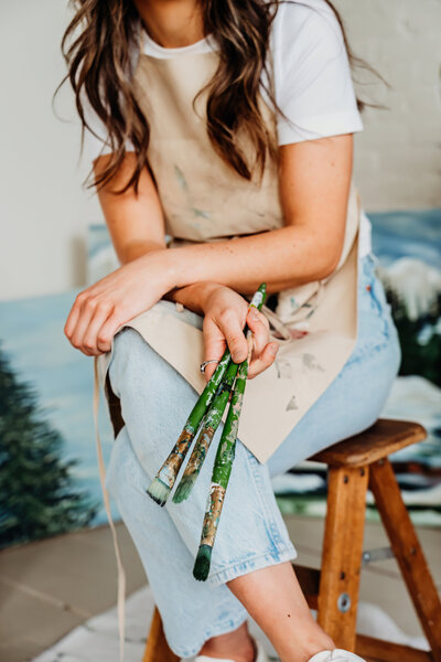 photo of a painter holding her paint brushes, paint brushes are in focus