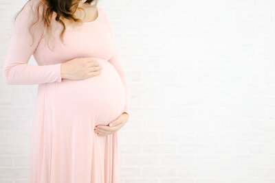 Mother with a long pink dress on holding her pregnant belly during maternity session with NH Newborn Photographer